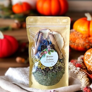 May include: A clear, resealable bag filled with a stovetop simmer pot blend. The bag contains cinnamon sticks, dried flowers, and herbs. A round sticker reads "Winter Solstice stovetop simmer pot". Pumpkins and candles are in the background.