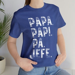 May include: A royal blue t-shirt with a white distressed graphic that reads "PAPA. PAPI. PA. JEFE."