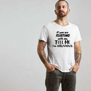 May include: White t-shirt with black text that reads "If you are FLIRTING with me, TELL ME. I'M OBLIVIOUS."