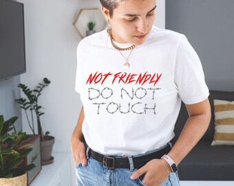 May include: White t-shirt with the text "NOT FRIENDLY DO NOT TOUCH" in black with barbed wire around the letters. The text "NOT FRIENDLY" is in red.