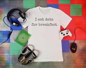 May include: A white t-shirt with the text "I eat data for breakfast" printed on it. The shirt is surrounded by gaming accessories, including a headset, a game controller, a mouse, and a game disc.