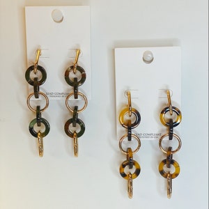 May include: Two pairs of gold and brown patterned hoop earrings. The earrings are made of multiple linked circles. The earrings are displayed on white cards with the text "Lead Compliant Designed in USA".