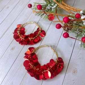 May include: A pair of gold hoop earrings with red sequin embellishments. The earrings are large and have a circular shape.