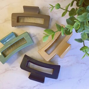 May include: Four plastic hair clips in different colors: brown, teal, beige, and navy blue. The clips are all the same shape, with a rectangular opening in the middle.