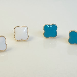 May include: Four gold-rimmed earrings with a clover design. Two earrings are white and two are turquoise.