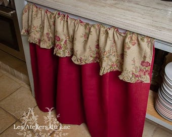 May include: A red and beige kitchen valance with a floral print and ruffled edges. The valance is hanging over a kitchen counter.