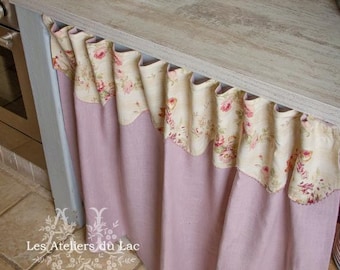 May include: A light wood countertop with a pink and floral patterned curtain hanging from the edge. The curtain is made of two layers of fabric, the top layer is a cream fabric with a floral pattern and the bottom layer is a solid pink fabric.