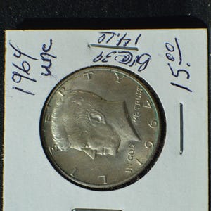 May include: A 1969 silver half dollar coin in a protective holder. The coin features a profile of a man and the words "IN GOD WE TRUST". The holder has handwritten notations.