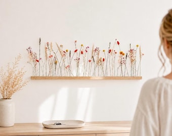 Puede incluir: Un estante de pared rectangular y alargado de madera que sostiene una variedad de flores y hierbas secas en tonos rojos, amarillos, rosas y beige. El arreglo presenta tallos finos y erguidos de flores silvestres y granos sobre la base.