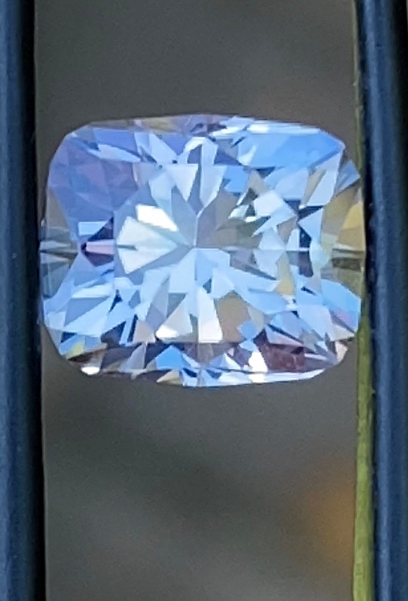 Op de afbeelding: Een heldere, gefacetteerde, rechthoekige edelsteen met een lichtblauwe tint. De edelsteen is gezet in een zilverkleurige zetting.