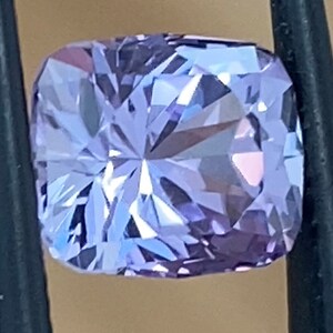 Op de afbeelding: Een lichtpaarse edelsteen met een kussen-slijpsel en vele facetten. De edelsteen wordt vastgehouden door een pincet.