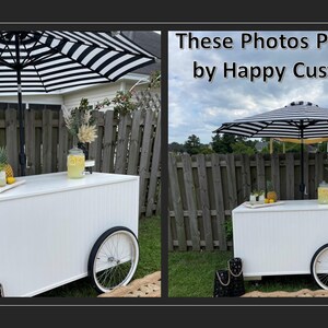 May include: Two white wooden bar carts with black and white striped umbrellas, set up outdoors with lemonade and pineapple garnishes.  "These Photos Provided by Happy Customer" text is visible in the image.