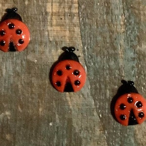 May include: Three red and black ladybug-shaped glass ornaments on a wood background.