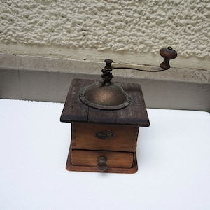 May include: A vintage wooden coffee grinder with a metal crank and a drawer for collecting the ground coffee. The grinder has a dark brown wooden body and a brass top.
