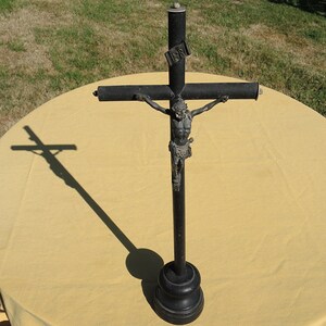 May include: A black crucifix with a wooden base and a metal Jesus figure. The crucifix is on a yellow tablecloth.