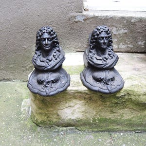 Puede incluir: Dos esculturas de hierro fundido negro que representan bustos con cabello rizado y cuellos ornamentados. Las esculturas están montadas sobre una base con un diseño floral. Los bustos están colocados sobre un escalón de piedra, ideal para decoración.