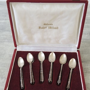 May include: A red velvet lined box with six silver teaspoons. The box has a gold clasp and the inscription "Orfevrerie Saint Medard" on the inside lid.