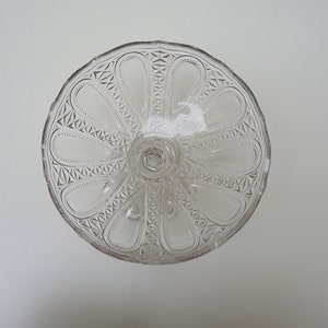 May include: A clear glass cake stand with a scalloped edge and a decorative pattern of ovals and diamonds.