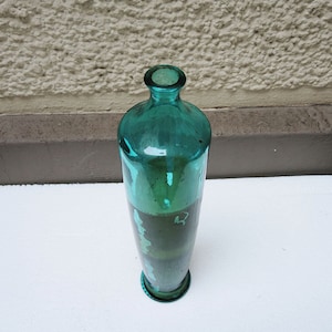 May include: A tall, teal blue glass bottle with a rounded bottom and a narrow neck. The bottle is empty and appears to be vintage.