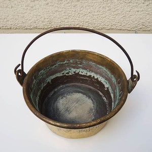 May include: A vintage brass pot with a worn handle. The pot has a green patina and is in good condition.
