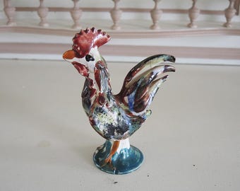 May include: A ceramic rooster figurine with a colorful, abstract design. The rooster is standing on a base with a blue and green glaze.