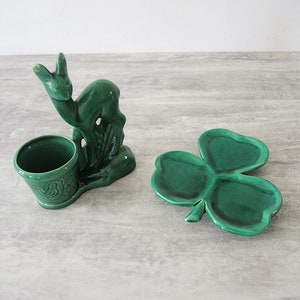 May include: A green ceramic deer figurine with a small green planter pot. The deer is standing on a green shamrock-shaped dish.