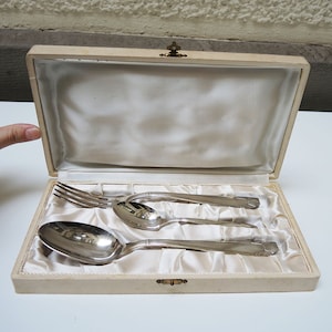May include: A set of silver-plated cutlery in a white box with a satin lining. The set includes a fork, a knife, and a spoon.
