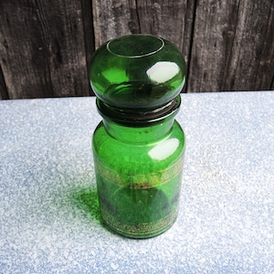 May include: A green glass jar with a gold design around the middle. The jar has a round, green glass lid.