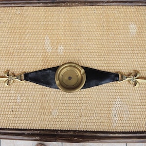 May include: A horizontal decorative object featuring a central circular brass ashtray mounted on a black leather strap. The strap is flanked on both sides by polished brass fleur-de-lis ornaments, creating a symmetrical design with metallic and dark leather elements.