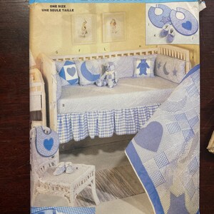 May include: A vintage sewing pattern for a baby's nursery set. The pattern includes instructions for making a crib skirt, a quilt, a pillow, a bib, and booties. The pattern is from Butterick and is number 5028. The pattern is for one size.