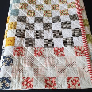 May include: A white quilt with a patchwork design. The quilt is made up of squares of different fabrics, including red, green, blue, and white. The quilt is quilted with a diamond pattern.