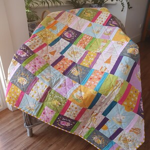 May include: A colourful patchwork quilt featuring a range of floral and animal prints. The quilt is made up of squares and rectangles of different fabrics, and it is edged with a yellow and white trim.