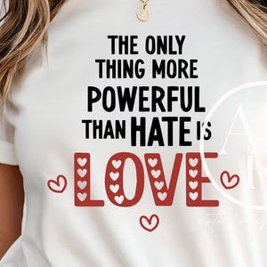 May include: White t-shirt with the text "THE ONLY THING MORE POWERFUL THAN HATE IS LOVE" in black and red. The word "LOVE" features heart-shaped designs. Small heart graphics are scattered around the text.