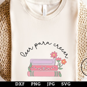 May include: A white t-shirt with the text "Leer para crecer" in black lettering, surrounded by a circle. Inside the circle are three stacked books with pink, purple, and green accents. The books are decorated with pink flowers.