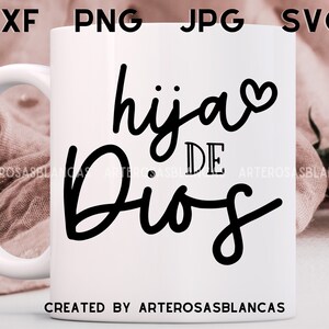 Puede incluir: Taza de cer&aacute;mica blanca con un dise&ntilde;o negro que dice "hija de Dios" con un peque&ntilde;o coraz&oacute;n al lado de la palabra "hija". La taza est&aacute; sobre una superficie de tela rosa.