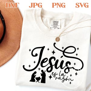 Peut inclure: T-shirt crème avec l'inscription noire "Jesús es la razón" et une silhouette de la nativité. Le t-shirt a un col rond et des manches courtes. Un collier doré avec un pendentif est visible.