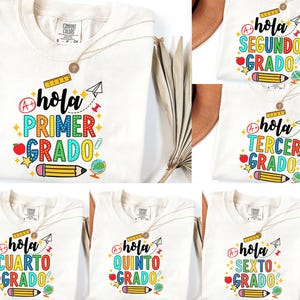 May include: Cream-coloured t-shirts with colourful text and graphics. Each shirt features the word "Hola" and a grade level, such as "Primer Grado" or "Segundo Grado." Designs include pencils, apples, stars, and globes. A necklace with a pendant is visible.
