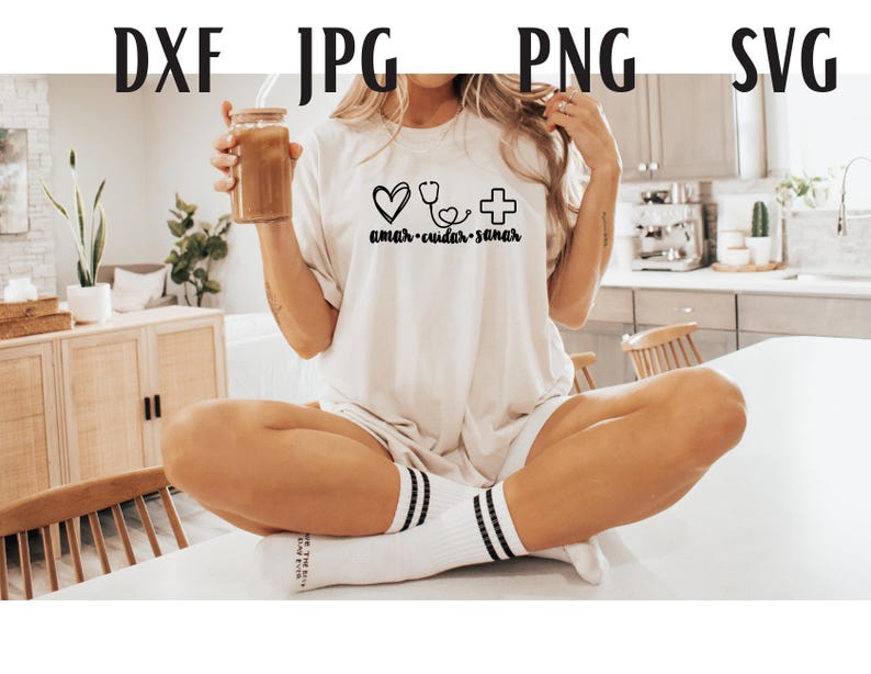 May include: A white t-shirt with a heart, stethoscope, and cross graphic and the text "amar - cuidar - sanar". The model is wearing the shirt and holding a glass of iced coffee.
