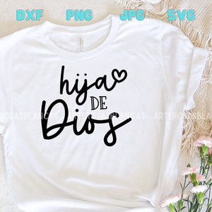 Puede incluir: Camiseta blanca con texto negro que dice "hija de Dios" con un peque&ntilde;o coraz&oacute;n rosa sobre la palabra "hija".