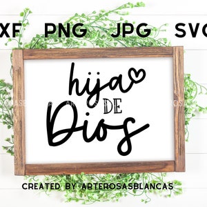 Puede incluir: Un letrero de madera blanco con marco marr&oacute;n, con el texto "hija de Dios" en letras cursivas negras con un peque&ntilde;o coraz&oacute;n sobre la palabra "hija". El letrero est&aacute; sobre un fondo de madera blanca con plantas verdes frondosas a cada lado.