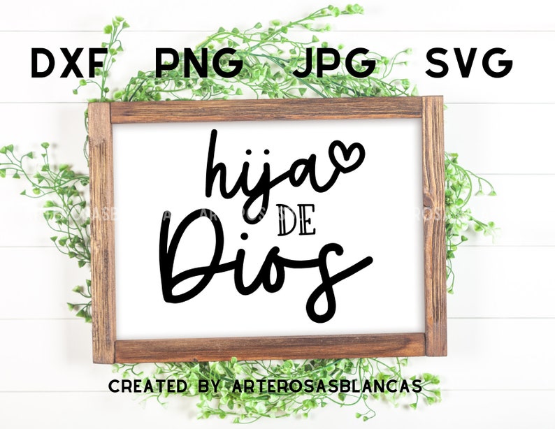 Puede incluir: Un letrero de madera blanco con marco marr&oacute;n, con el texto "hija de Dios" en letras cursivas negras con un peque&ntilde;o coraz&oacute;n sobre la palabra "hija". El letrero est&aacute; sobre un fondo de madera blanca con plantas verdes frondosas a cada lado.