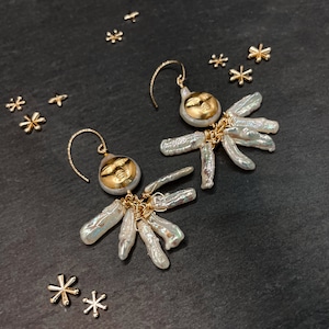 May include: Gold-toned dangle earrings featuring a face design with a pearl cluster. The earrings have a gold hook and are accented with small gold star-shaped charms. The pearls have a subtle iridescent sheen.