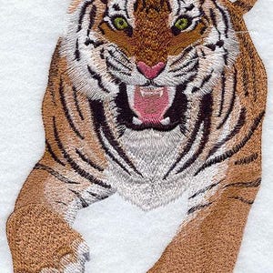 May include: Embroidered tiger design with brown and black stripes, green eyes, and a pink nose. The tiger is depicted with an open mouth, revealing teeth, and outstretched paws. The artwork is on a white background.