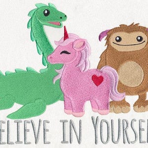 May include: Embroidered design featuring a green dragon, a pink unicorn with a heart, and a brown yeti. The phrase "BELIEVE IN YOURSELF" is stitched below the characters in gray thread. The design is on a white background.