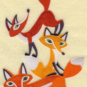 May include: Embroidered design featuring three stylized foxes in shades of orange, white, and black. The foxes have green eyes and are arranged in a playful, stacked composition against a light yellow background. The design is likely for a textile or craft project.