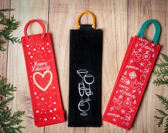 May include: Three red and black wine bottle gift bags with different holiday designs. The bags have handles and are made of burlap. The designs include a heart with the words "Happy Holidays", a set of glasses, and a snowman with the words "Merry Christmas".