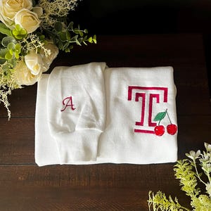 May include: White sweatshirt with a red embroidered letter 'A' on the left sleeve and a red embroidered 'T' with cherries on the right side.