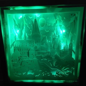 May include: A green illuminated papercraft of Hogwarts castle with lightning bolts and bats in the background.