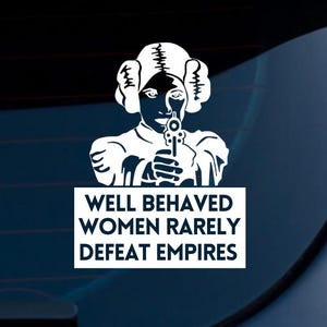 Puede incluir: Calcomanía de vinilo blanco que presenta una imagen estilizada de una mujer sosteniendo un blaster, con el texto "WELL BEHAVED WOMEN RARELY DEFEAT EMPIRES" en un recuadro rectangular. Diseñada para aplicar en una ventana de coche o superficie similar.