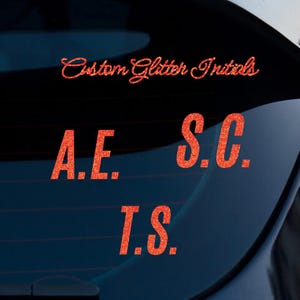 Puede incluir: Calcomanías de purpurina naranja con el texto "Custom Glitter Initials", "A.E.", "S.C." y "T.S." se muestran sobre un fondo oscuro. Las calcomanías están en una fuente de escritura y letras de bloque.